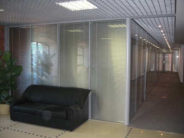 Одинокий кожанный диван на фоне стеклянной офисной перегородки